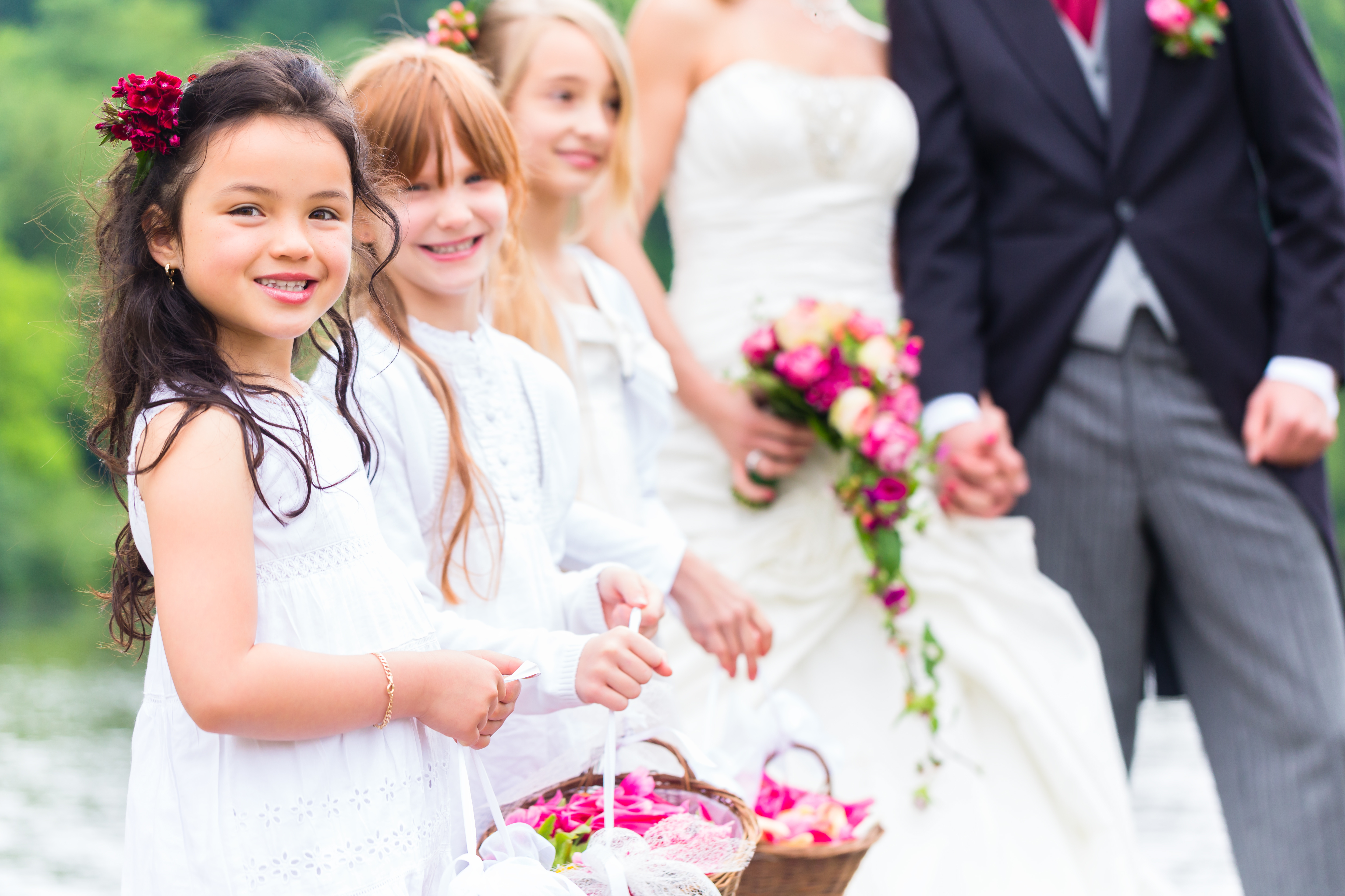 flower girls in white standing with a basket full of flowers