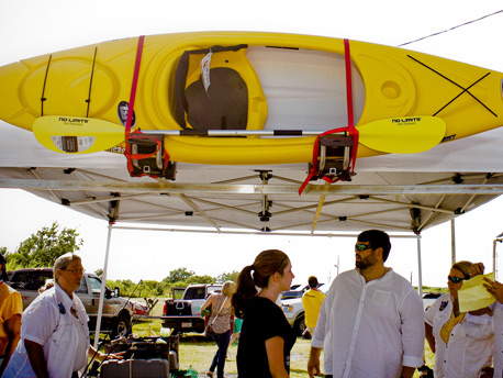 Yellow kayak sitting on top of booth at outdoor event with crowd