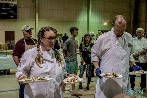 two chefs carry dishes to judges table for critique