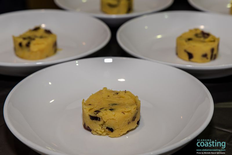 group of white dishes professionally plated with yellow polenta-like disk in center