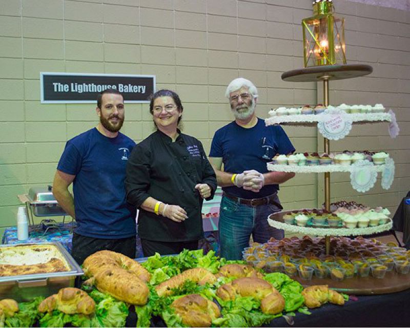 Chefs from Lighthouse Bakery standing behind their booth table in convention hall
