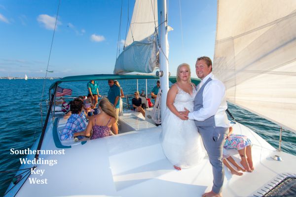 Wedding couple pose for photos on the bow of their private sunset sailboat reception by Southernmost Weddings Key West