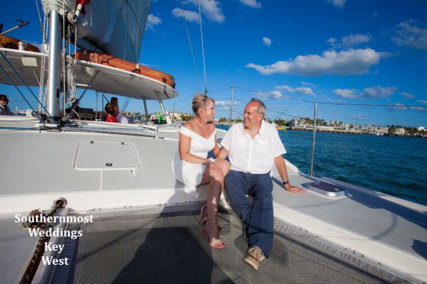 Wedding couple sit on the bow of their private charted catamaran after their beach wedding by Southernmost Weddings Key West