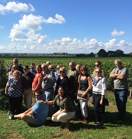 Group of people standing in front of a vineyard on a sunny day