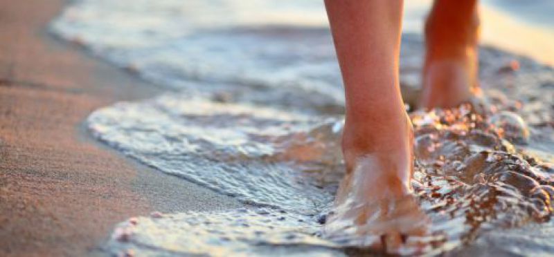 image of a persons feet walking on the beach when the water comes on shore