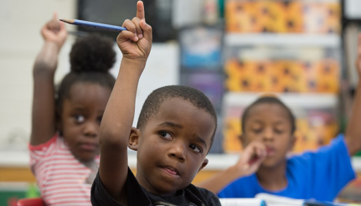 3 children raising their hands in a classroom