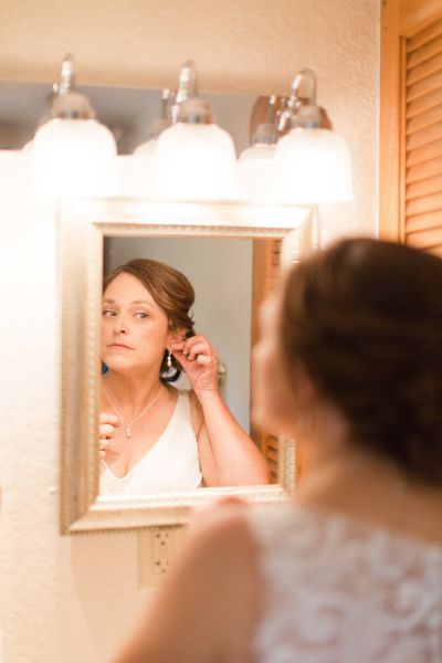 Bride putting on her earrings in the mirror