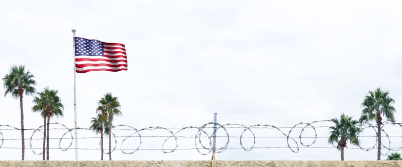 Image of American Flag behind a wall of barbwire